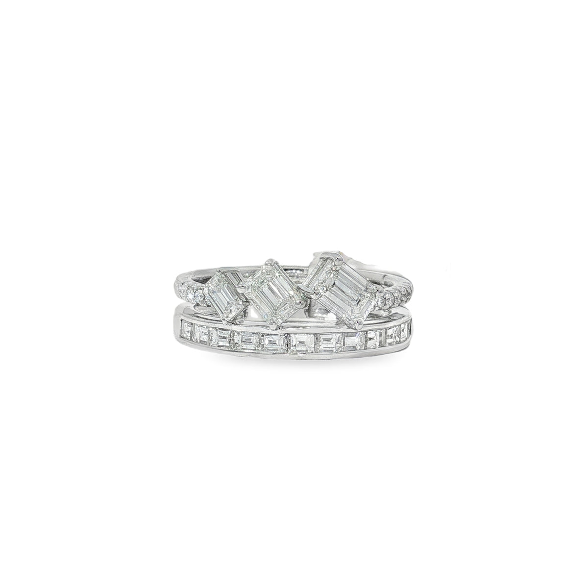 White gold ring with three tilted emerald-cut diamonds above a baguette diamond band